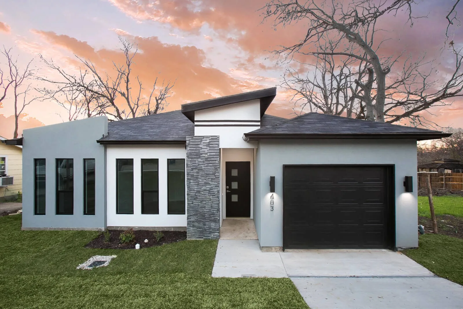 403 Avenue Dallas, a modern single story house with stacked stone and a black garage door at dusk