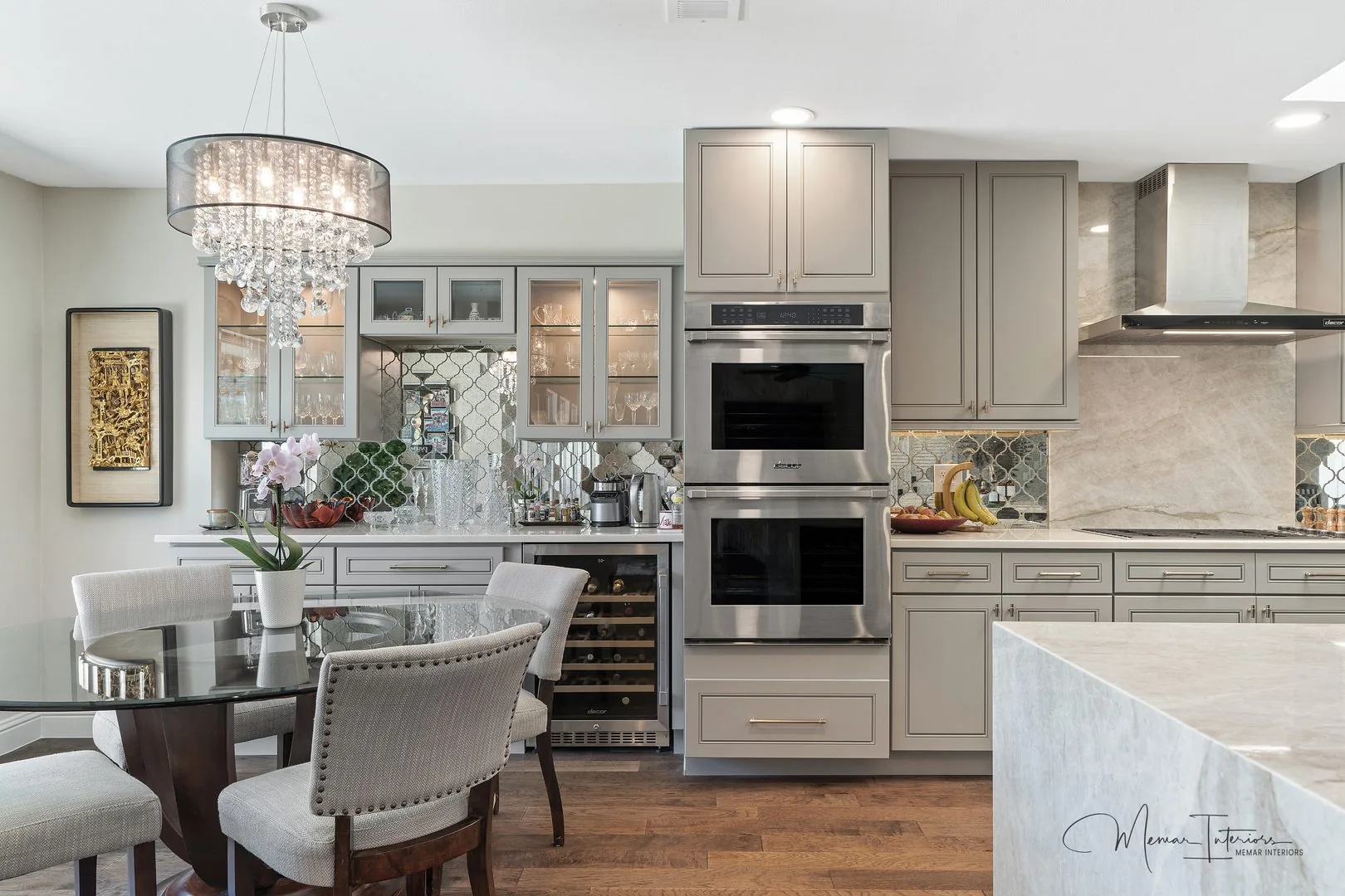 A grey kitchen with a crystal chandelier, mirrored backsplash and stone counters