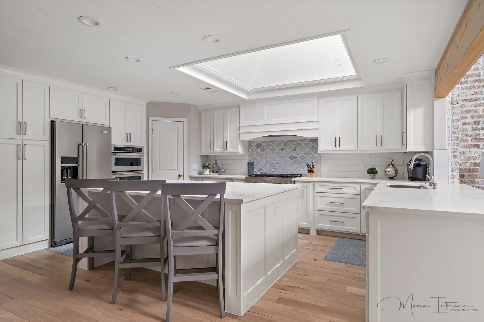 A white kitchen with a skylight, shaker cabinetry and a marble waterfall island