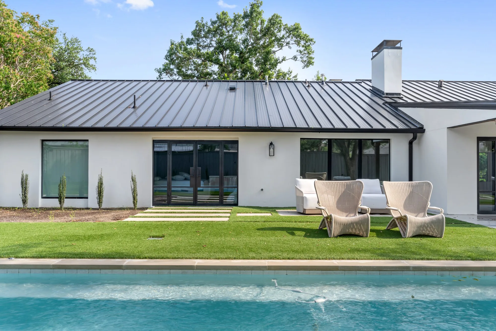 The rear elevation of a white Memar Interiors house, with folding glass doors opening onto a lawn and pool