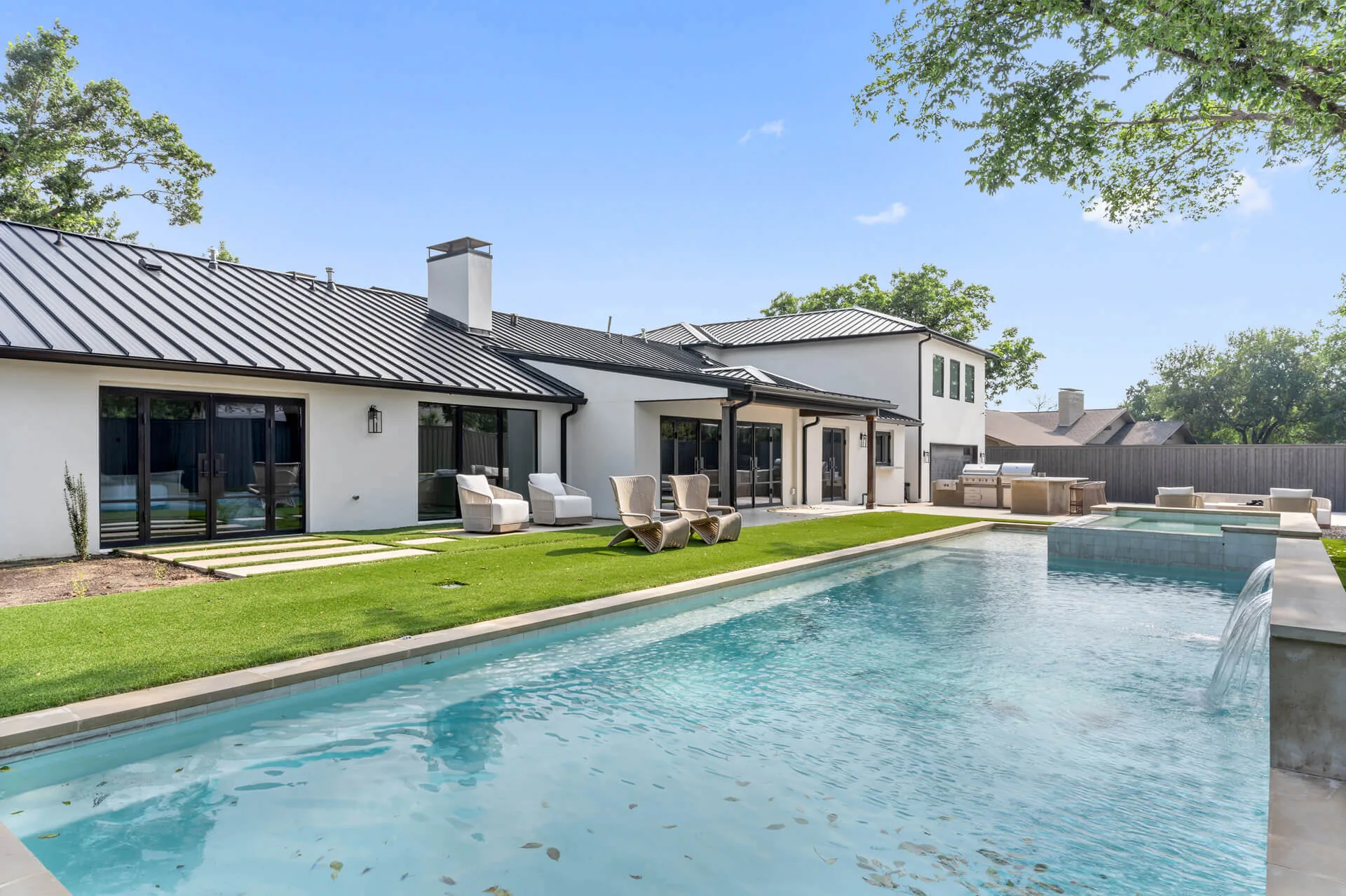 Preston Hollow Home, a white Memar Interiors residence with a standing seam metal roof beside a long pool